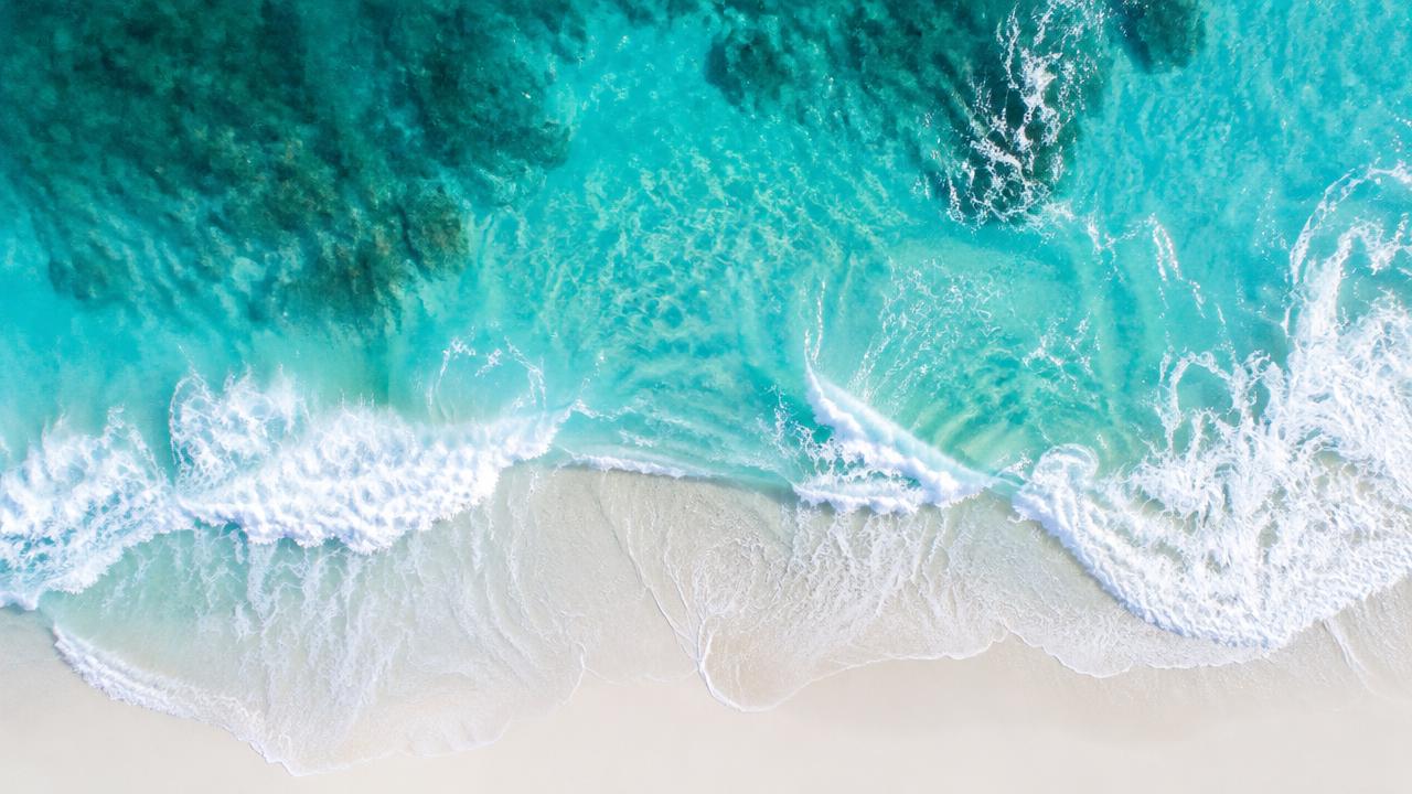 Aerial drone photo of turquoise waves meeting white sand beach, abstract patterns from above