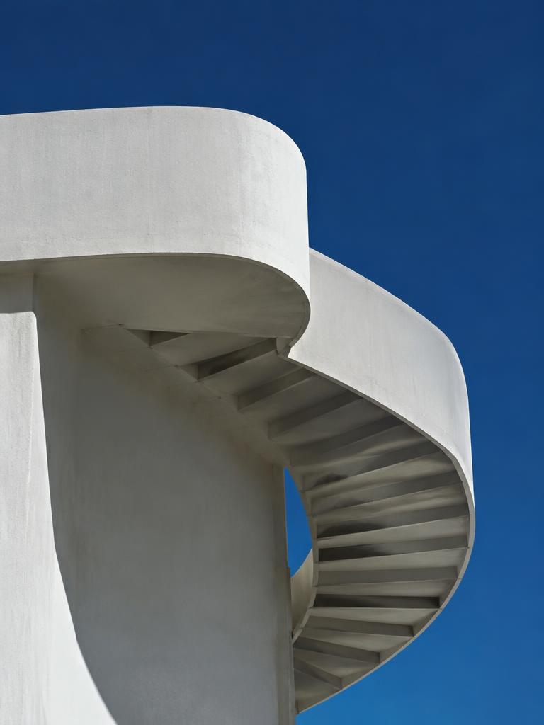 Minimalist white concrete spiral staircase against deep blue sky, harsh shadows, geometric composition